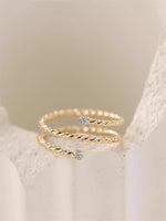Gold filled twisted ring with moissanite accents on a light beige stone background