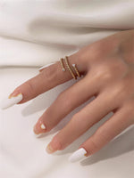 Gold filled twisted ring with moissanite accents on a models hand with the white cloth background