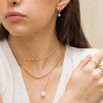 Close-up of a woman wearing gold necklaces and earrings with a neutral background