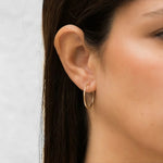 Close-up of a person wearing a gold hoop earring against a white background