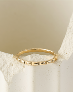 Gold filled ring with a textured band on a beige stone background