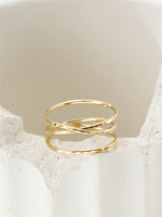 Gold filled ring with a criss-cross design on a textured beige surface