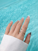 Hand with two gold filled rings against a turquoise water background