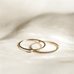 Two rings, one with the opal and the other twisted rope like style on the white cloth background