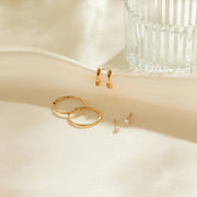 Set of gold hoop earrings on a soft beige surface with a glass container in the background.