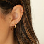 Close-up of an ear wearing gold hoop earrings with a neutral background