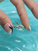 Gold filled ring held by a hand with a black and white nail design against a blue water background